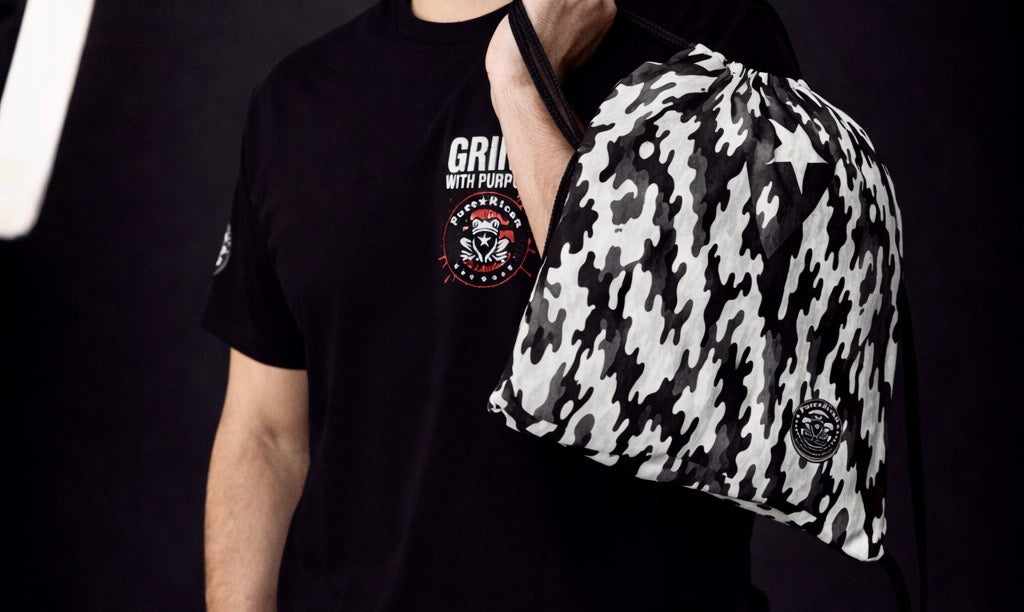 Close-up of hand holding Pure⭐️Rican black and white camo drawstring bag with Boricua star and logo in studio lighting