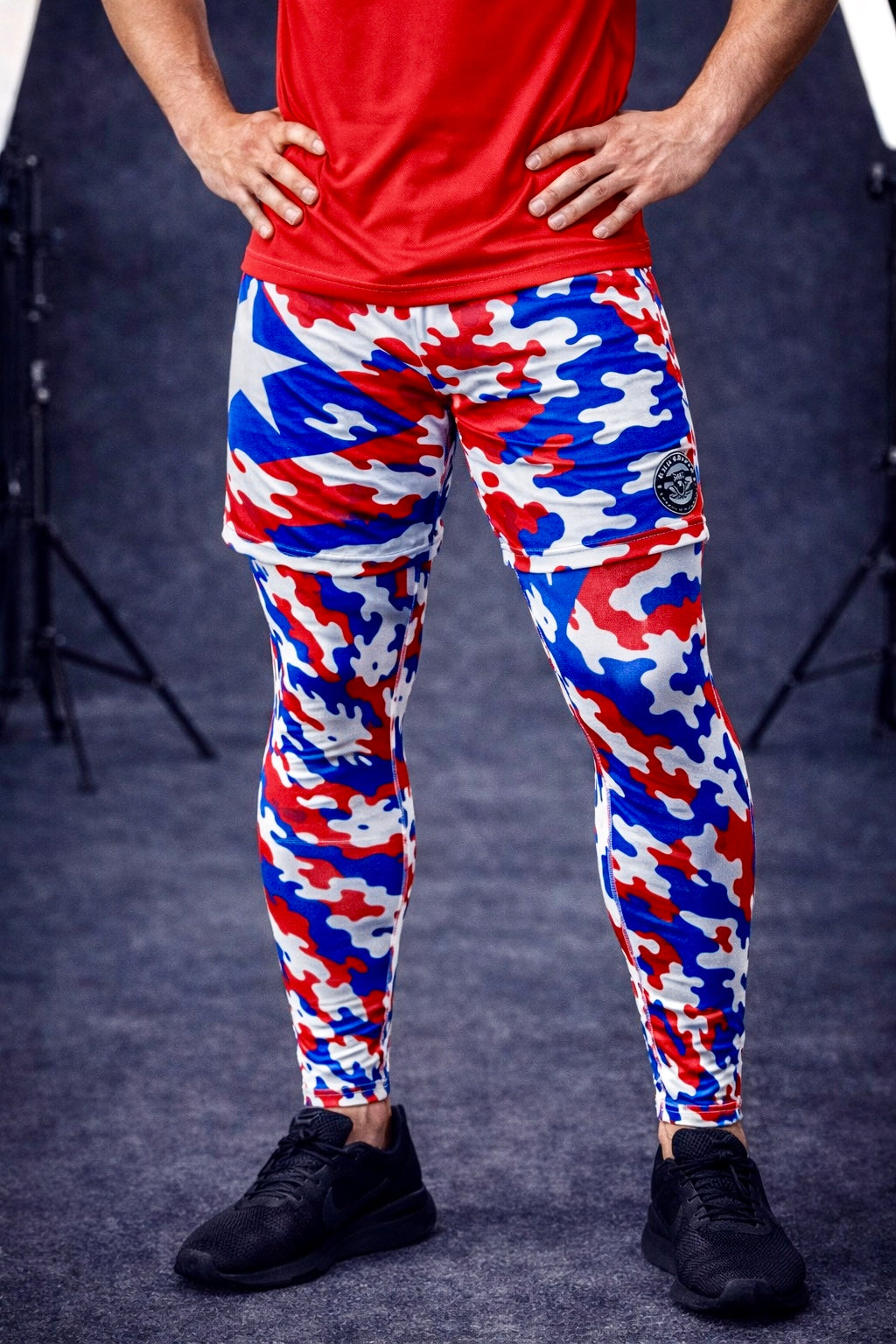 Person wearing red shirt and multicolored camouflage pants on a dark background