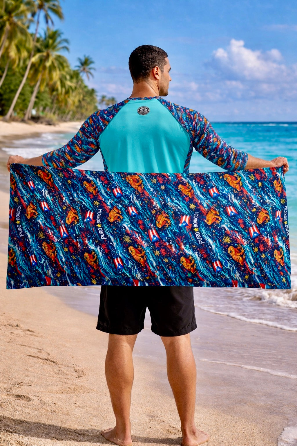 Male model wearing turquoise rash guard holding Pure⭐️Rican towel behind back on tropical shoreline