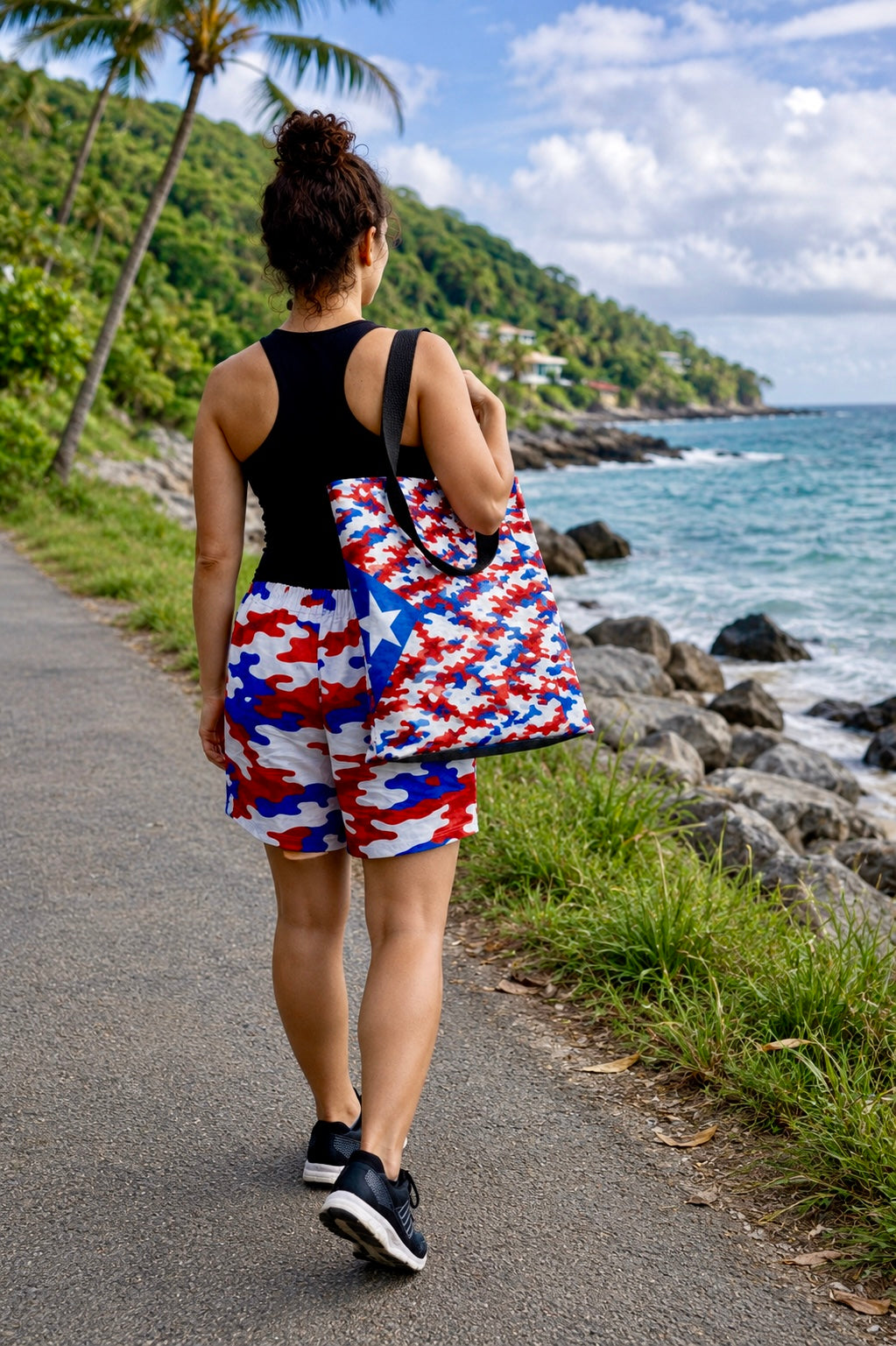 Woman walking along a tropical coastline carrying the Pure⭐️Rican Patriotic Camo Boricua tote bag with matching Puerto Rican camo shorts during a beachside walk.